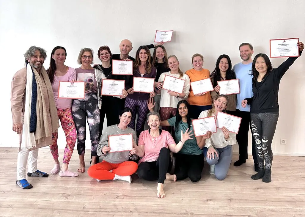A smiling group of yoga students holding up their certificates