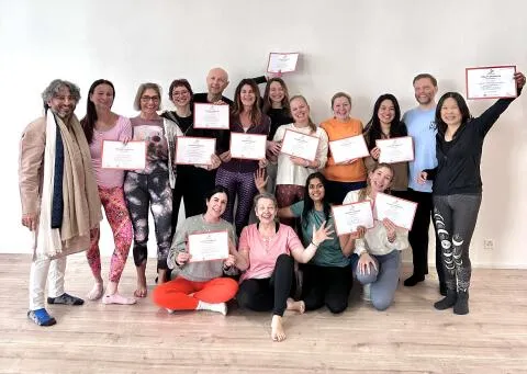 A smiling group of yoga students holding up their certificates