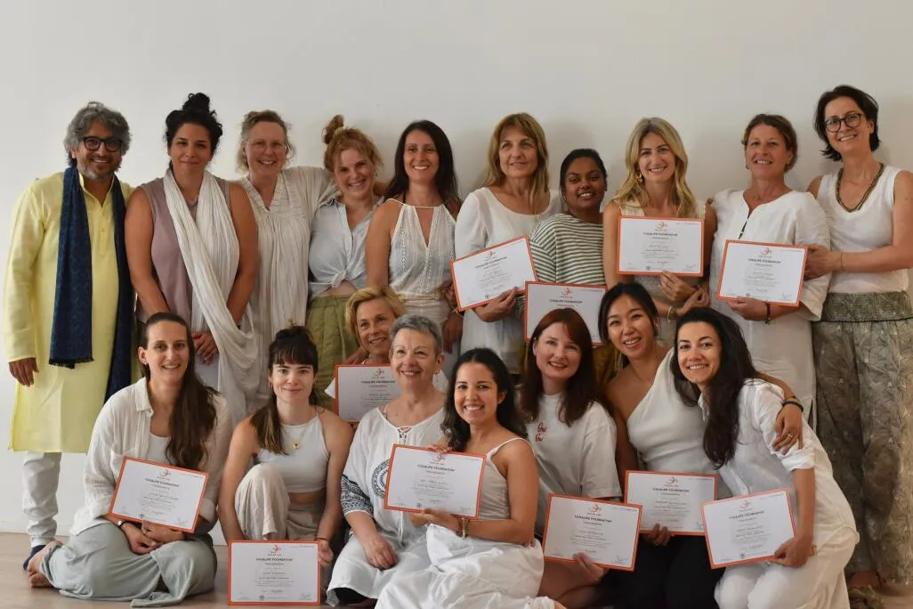 A large group of graduates in white clothing holding certificates