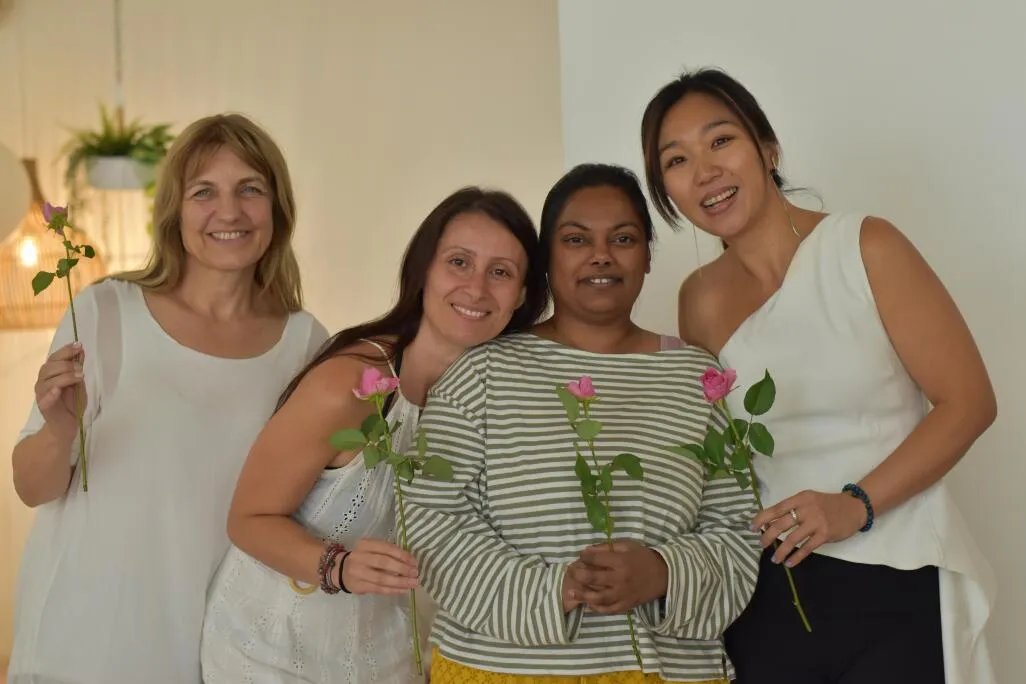 Four smiling women standing together and holding pink roses