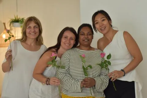 Four smiling women standing together and holding pink roses